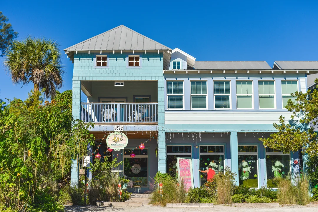 light blue building with a colorful storefront, surrounded by palm trees, and located on Pine Avenue in Anna Maria Island.